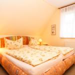 Doppelbett mit floraler Bettwäsche, Nachttische und Fenster mit Vorhängen.