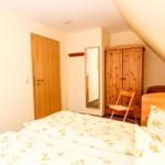 Schlafzimmer mit Bett, Kleiderschrank und Spiegel unter Dachschräge.