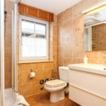 Badezimmer mit Dusche, Toilette und Waschbecken. Fenster mit Jalousie und Spiegel.