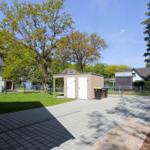 Hinterhof mit Pavillon, Mülltonnen und Grünfläche. Wohnhaus und Bäume im Hintergrund.