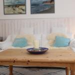 Ein Wohnzimmer mit weißem Sofa, Holztisch und Strandmotiven an der Wand.