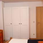 Schlafzimmer mit weißen Schrank, Holztür und Kinderbett mit orangefarbenem Bettzeug.