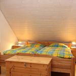 Doppelbett mit grün-gelbem Bettzeug, zwei Nachttische mit Lampen, Holzdecke und Fenster mit Vorhang.