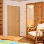 Schlafzimmer mit Holzbett, Stuhl und Kleiderschrank. Tür und Wand sind sichtbar.