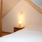 Schlafzimmer mit Dachschrägen, Bett und Nachttisch mit Lampe.