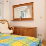 Schlafzimmer mit Bett, Stuhl, Spiegel und Holzschränkchen.