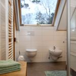Badezimmer mit Toilette, Waschbecken und Dusche. Fenster mit Blick auf Bäume.