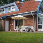 Haus mit Terrasse, Tisch, Stühlen und Sonnenschirm. Garten und Strandkorb sind vorhanden.