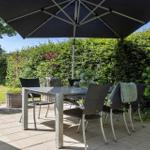 Terrasse mit Tisch, Stühlen und Sonnenschutz. Hintergrund: grüne Hecke und Garten.