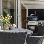 Terrasse mit Tisch, Stühlen, Grill und Blumenarrangement.