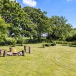 Grüner Garten mit Feuerplatz und Baumstumpf-Sitzgelegenheiten unter Bäumen.