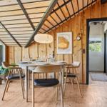 Esszimmer mit Holzwand, Tisch und Stühlen, Glasfront und Bücherregal.