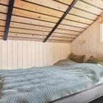 Schlafzimmer mit Bett, Holzwand und Dachbodenstruktur. Fenster mit Blick auf Grün.
