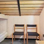 Zimmer mit Schlafcouch, zwei Stühlen und Holzwänden.