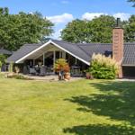 Moderne Villa mit Terrasse, Grill und Garten. Roter Schornstein und grüne Bäume im Hintergrund.