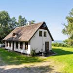 Wohnhaus mit Strohdach, Garten und Blick auf Wasser.