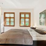 Schlafzimmer mit Bett, zwei Fenstern und Kleiderschrank. Wandbild an der Wand.