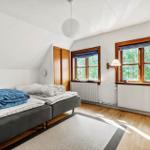 Schlafzimmer mit Doppelbett, Holzboden und zwei Fenstern mit Blick auf Bäume.