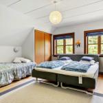 Zimmer mit Doppelbett und Einzelbett, Holzboden und zwei Fenster mit Blick auf Bäume.