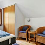 Schlafzimmer mit Bett, zwei Rattanstühlen und einem Fenster mit Blick auf die Natur.