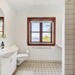 Badezimmer mit Waschbecken, Toilette und Dusche. Fenster mit Blick auf Wasser.