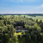 Haus mit Dach und weißen Wänden inmitten von Wald und Feldern.