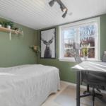 Schlafzimmer mit Bett, Schreibtisch und Fenster. Wandfarbe grün, Decke weiß. Pflanzen und Bild an der Wand.