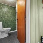 Toilettenbereich mit Palmen壁纸 und Holztür. Grüne vertikale Wandverkleidung und Kleiderhaken.