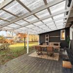 Terrasse mit Holztisch, Stühlen und Dachkonstruktion. Hintergrund: Garten und Hauswand.