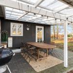 Terrasse mit Tisch, Stühlen und Grill unter einem weißen Dach.