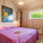 Schlafzimmer mit Holzwänden, Bett mit rosa Bettwäsche und Wandbild von Vincent van Gogh.
