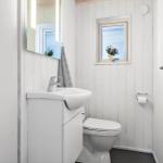 Badezimmer mit Waschbecken, Toilette und kleinem Fenster mit Blumen.