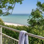 Blick von Balkon auf Strand und Meer durch grüne Bäume und Sträucher.