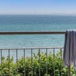 Balkon mit Blick auf das Meer und Windkraftanlagen im Hintergrund. Ein Handtuch hängt am Geländer.