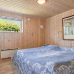 Schlafzimmer mit Holzwandverkleidung, Bett mit blauem Tagesdecke und Fenster mit Blick auf Bäume.