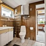 Badezimmer mit Waschbecken, Toilette und Badewannenheizung. Holzwandverkleidung und Fenster mit Blick.