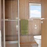 Badezimmer mit Dusche, Toilette und Waschmaschine. Holzwände und kleines Fenster.