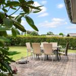 Terrasse mit Sitzgruppe, Grill und Grünfläche. Blick auf Hecke und Himmel.