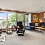 Wohnzimmer mit Sofa, Sessel und Kamin. Große Fensterfront mit Blick auf Garten.