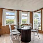 Esszimmer mit Glas-Tisch, weißen Stühlen und Holzwänden. Große Fenster mit Blick nach draußen.