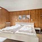 Schlafzimmer mit Holzwand, weißem Bett und Fenster. An der Wand hängen drei Bilder.