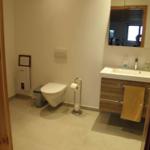 Badezimmer mit Toilette, bodentiefer Dusche, Wandwaschbecken und 2 Schubladen, in denen sich Handtücher und diverse andere Dinge befinden