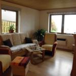 Wohnzimmer mit Sofa, Sesseln, Couchtisch und Pflanzen. Holzfußboden und Fenster mit Blick.