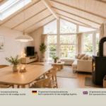 Ein Raum mit Essbereich und Wohnbereich. Holztisch, Sofa und Kaminofen sind sichtbar.