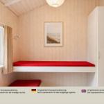 Schlafzimmer mit rotem Bett, Holzwand und Fenster mit Blick auf Wald.
