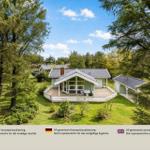 Ein Haus mit Terrasse und Garten inmitten von Bäumen unter blauem Himmel.