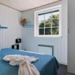 Schlafzimmer mit Bett, Fenster und Wandregal. Wandverkleidung und blaues Bettzeug.