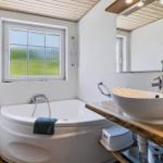 Bad mit Badewanne, Waschbecken und Fenster mit Blick auf Gras.