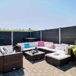 Terrasse mit Sitzgruppe, Tisch und Pflanze. Hintergrund: Holzumzäunung und Himmel.