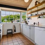 Küche mit Holzdecke, großen Fenstern und Küchenzeile mit Spüle und Geschirr.